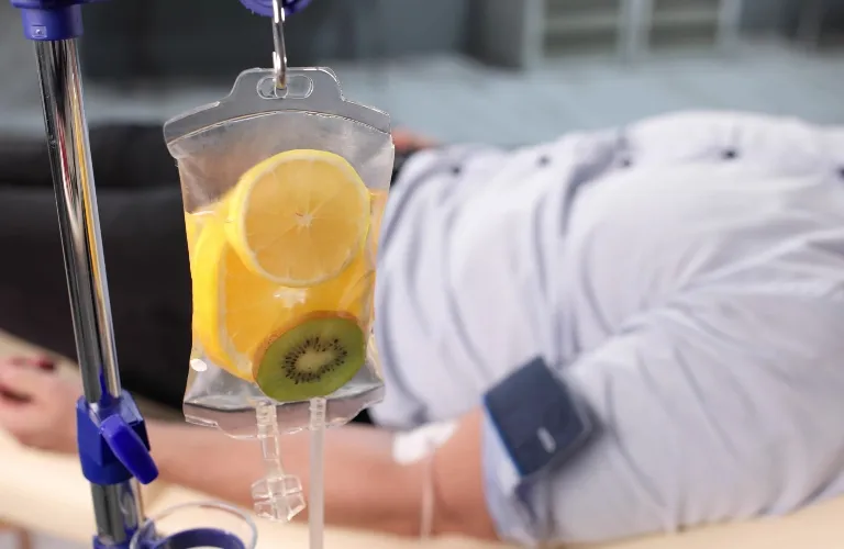 Intravenous drip bag containing lemon and kiwi slices with a patient lying in the background.