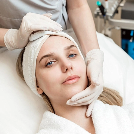 Woman receiving facial treatment from a gloved professional in a clinical setting.