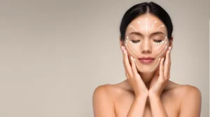 Young woman with closed eyes and skincare massage lines drawn on face, neutral background.