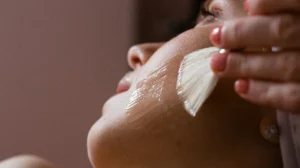 Close-up of a person receiving a facial treatment with a brush applying a clear gel on the cheek.