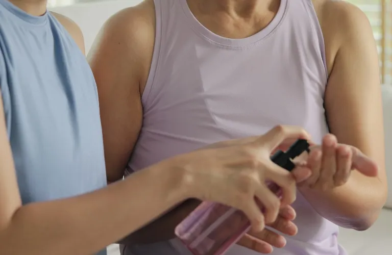 Two individuals in sleeveless tops applying hand sanitizer from a pink pump bottle.