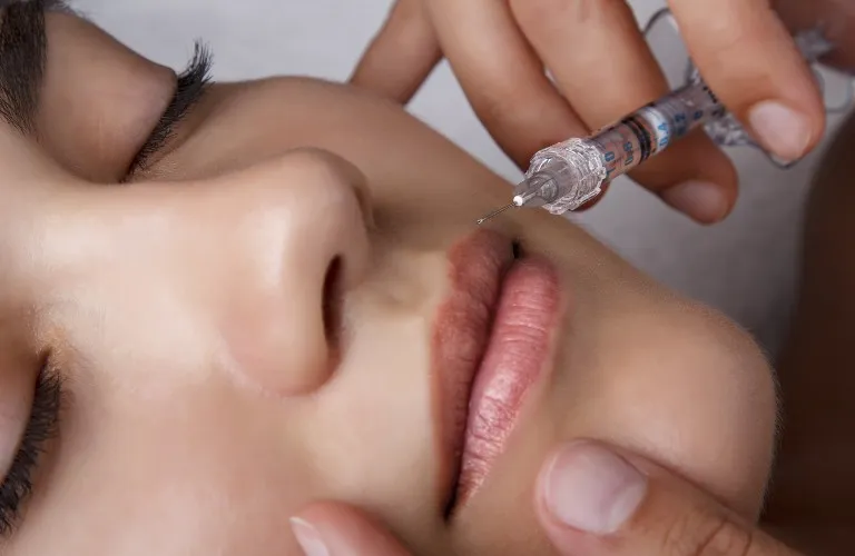 Close-up of a person receiving a lip injection with a syringe held by a medical professional.