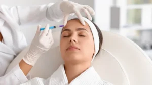 Medical professional wearing gloves administering cosmetic injection to woman's forehead in clinic.