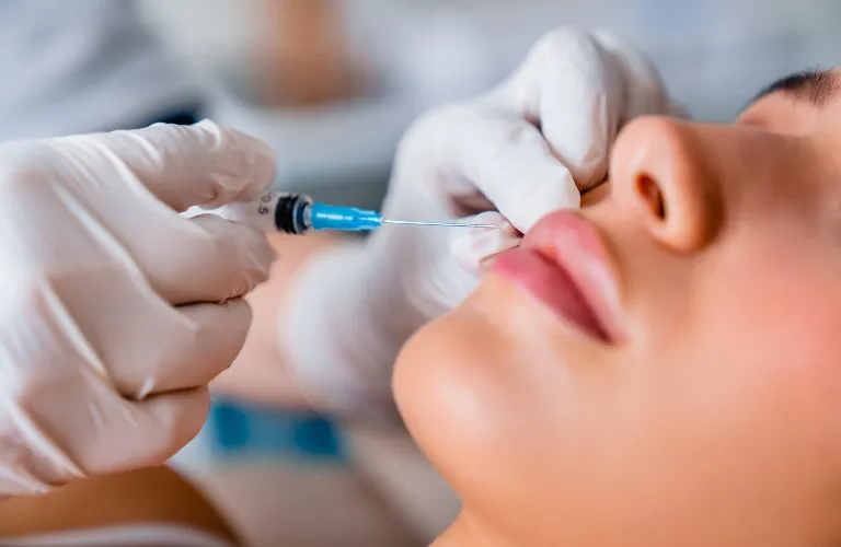 Close-up of a medical professional wearing white gloves administering a lip injection with a syringe.