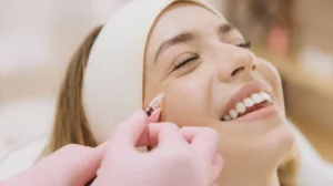 Close-up of a woman receiving a cosmetic injection near her eye, wearing a white headband.