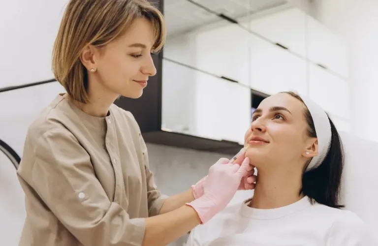 A professional skincare specialist wearing pink gloves examining a female client's face in a clinical setting.